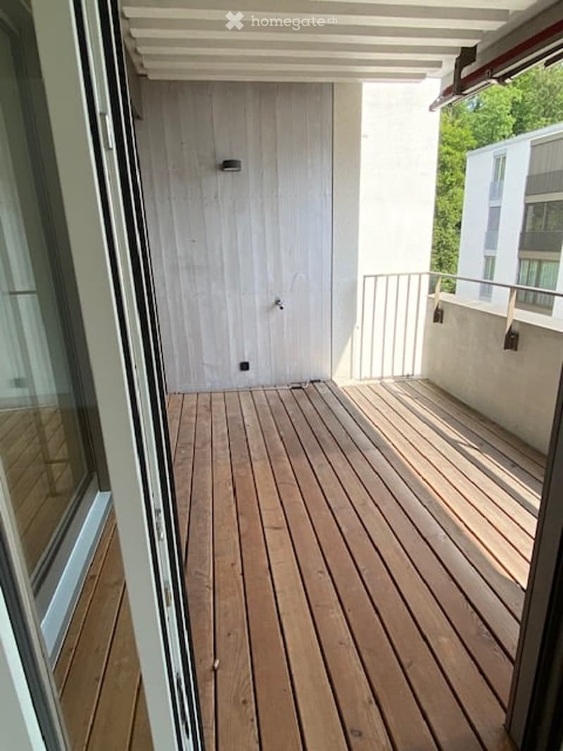 Wooden deck balcony with white walls, metal railing, and a sliding glass door leading inside.