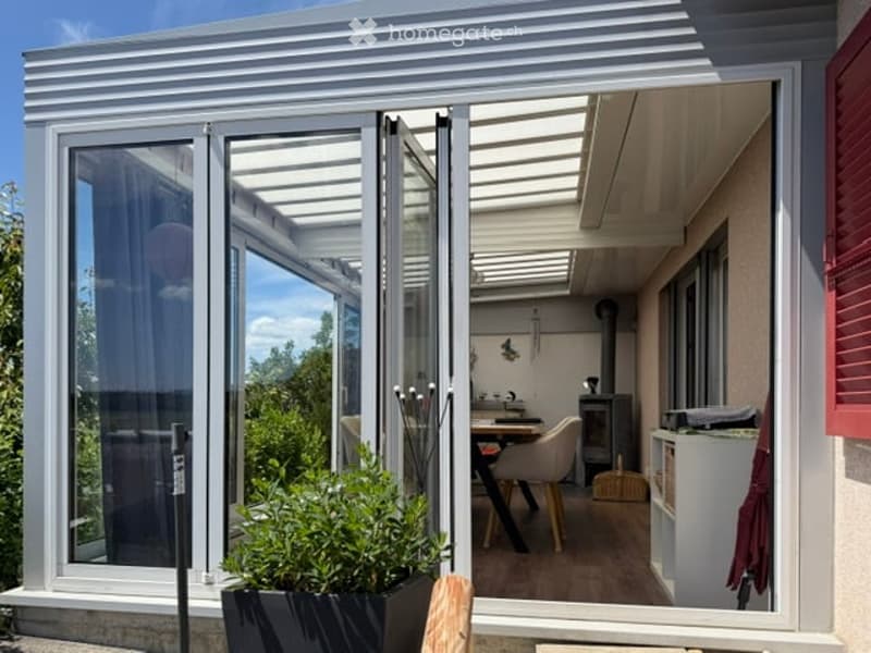 Modern balcony with large glass doors, wooden floor, and a small seating area with a table and chairs.