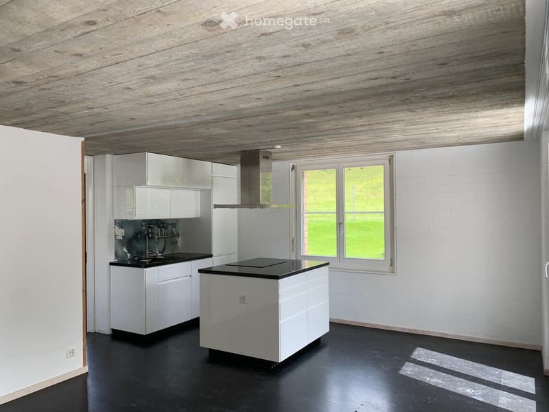 Modern kitchen with white cabinets, black countertops, island, and stainless steel range hood. Exposed wooden ceiling and white brick walls.