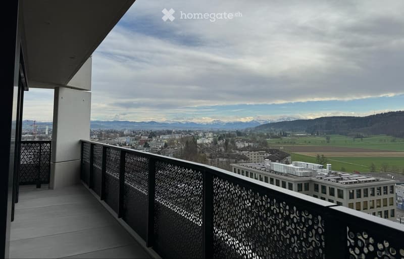 Balcony with a modern metal railing, overlooking a cityscape and distant mountains under a partly cloudy sky.