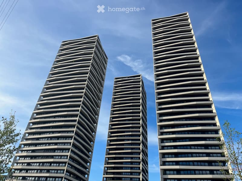 Four modern high-rise buildings with a sleek, tiered design and numerous windows, set against a clear blue sky.