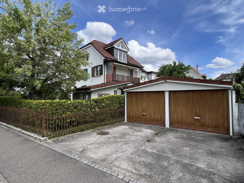 Two-story house with red-tiled roof, white walls, and a wooden garage with double doors.