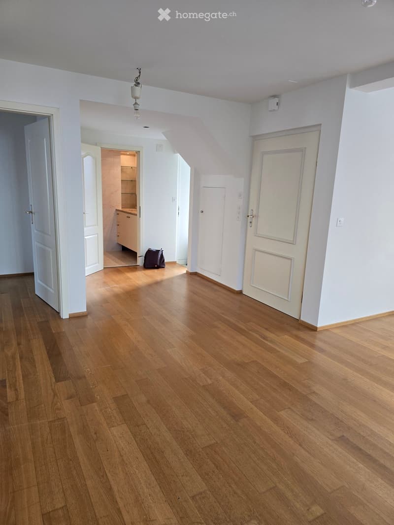 Empty room with wooden flooring, white walls, and several doors leading to other rooms. A small bag is placed near the doorway.