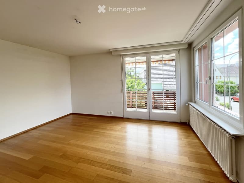 Empty room with wooden flooring, large windows, and a sliding glass door leading to a balcony area.