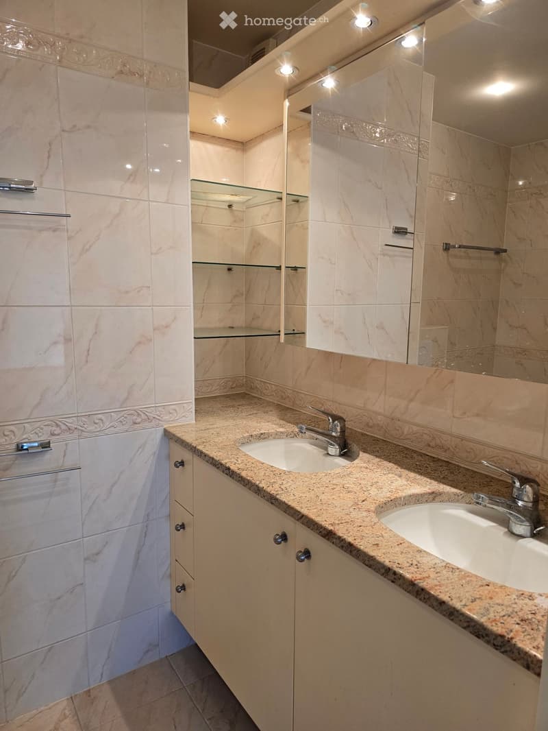 Modern bathroom with marble tiles, double sink vanity, mirrored cabinet, and recessed lighting.