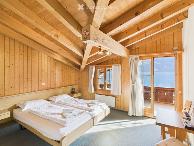 Cozy wooden bedroom with two single beds, nightstand, table, and a large window offering a scenic view.