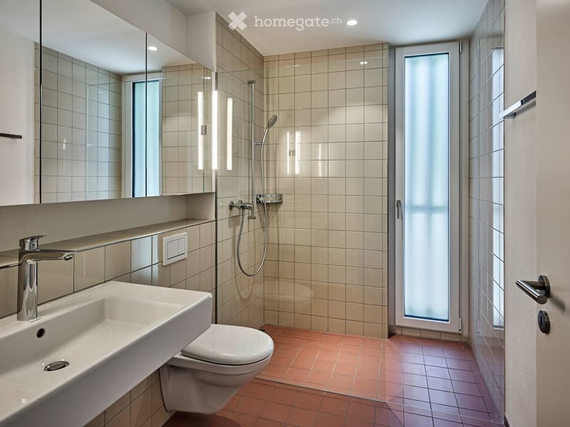 Modern bathroom with beige tiled walls, a white sink with a chrome faucet, a toilet, a large mirror, and a glass-enclosed shower area.