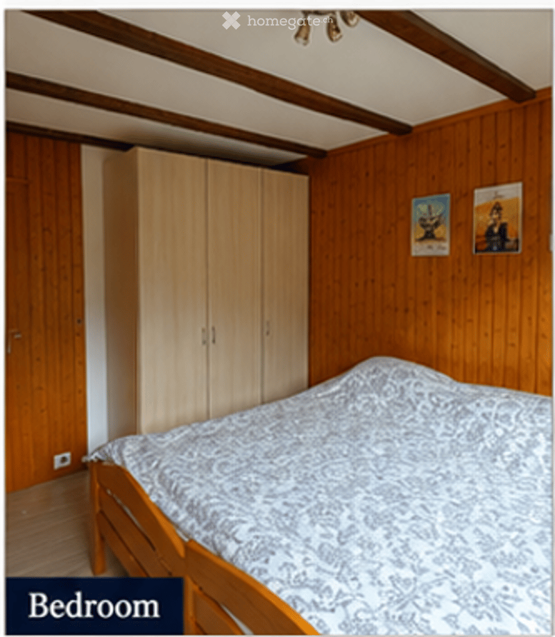 Cozy bedroom with wooden walls and ceiling beams, a neatly made bed with patterned bedding, a built-in wardrobe, and two framed pictures on the wall.