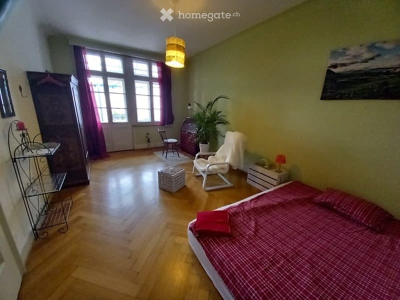 Bedroom. Cozy bedroom with wooden flooring, large windows with purple curtains, a bed with a red checkered duvet, a white armchair, a small table, a wardrobe, and a potted plant.