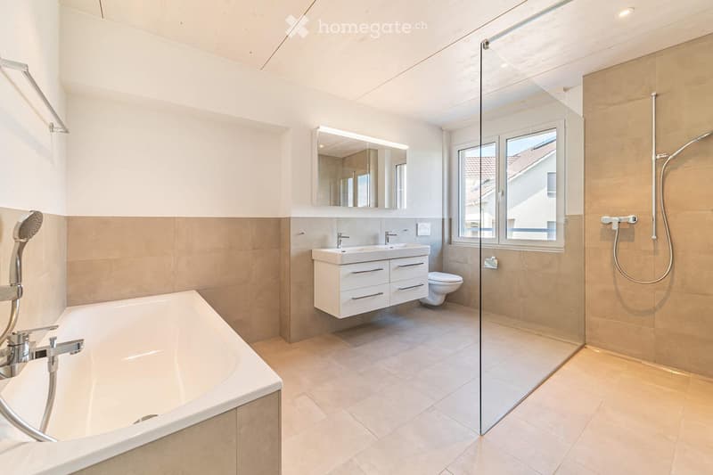 Modern bathroom with a bathtub, double sink, toilet, large mirror, and a glass-enclosed shower area.