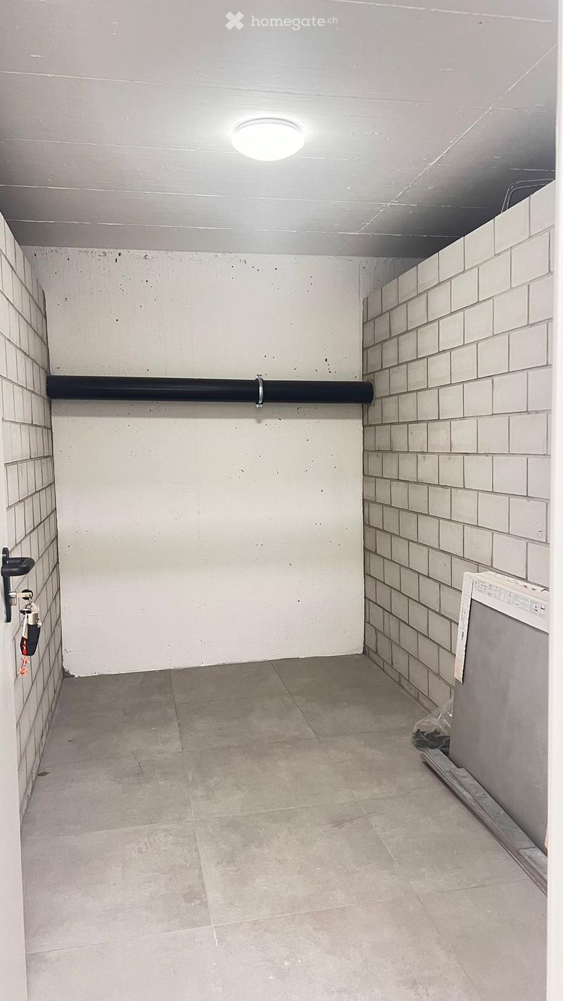 Empty hallway with tiled walls, concrete floor, and a single light fixture on the ceiling. A black pipe runs along the wall, and a door is visible on the left side.
