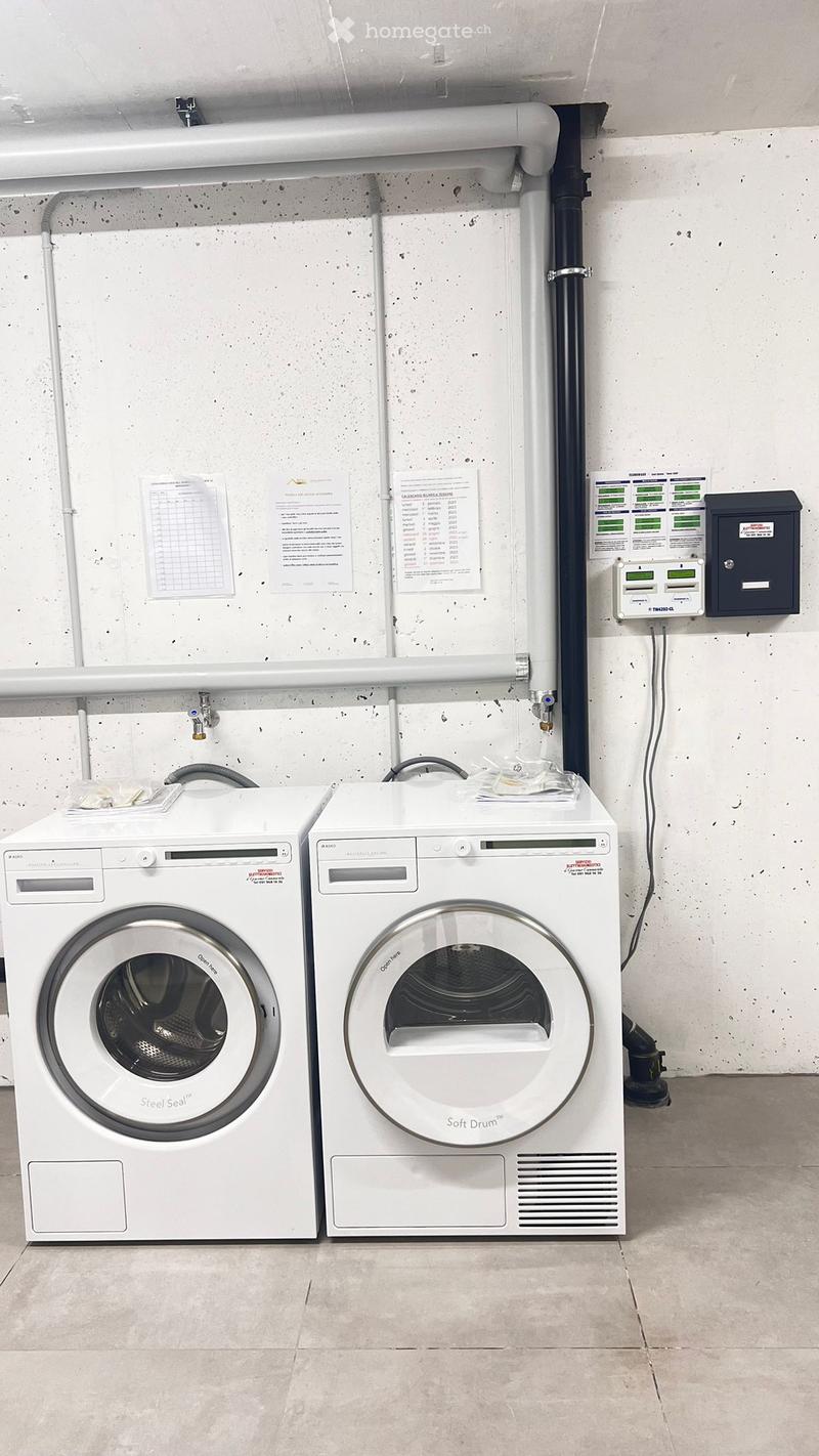 A clean, modern utility area featuring a white washing machine and dryer, with visible control panels and a control box on the wall.