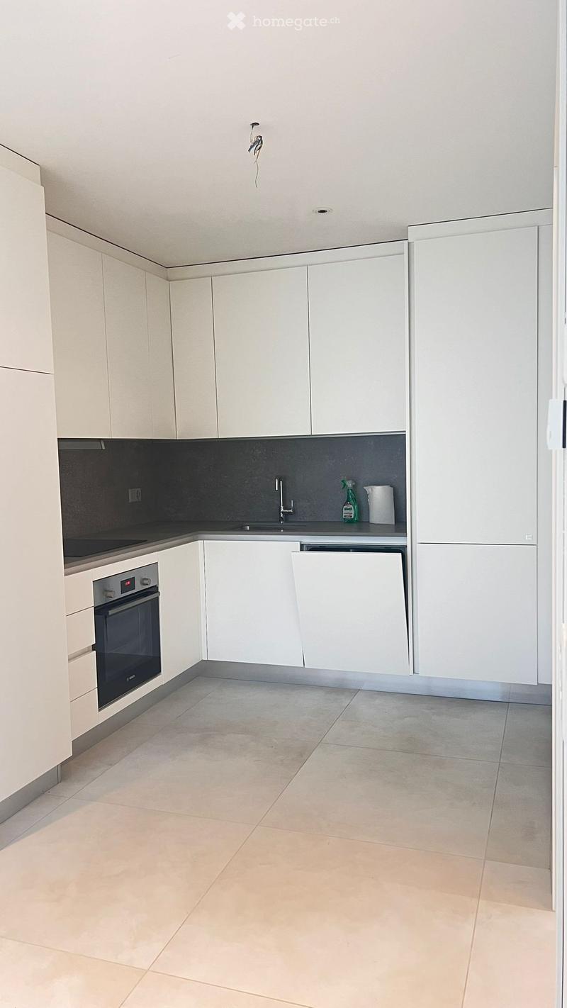 Modern kitchen with white cabinets, a built-in oven, a sink with a faucet, and a countertop with a few items including a bottle and a paper towel roll.