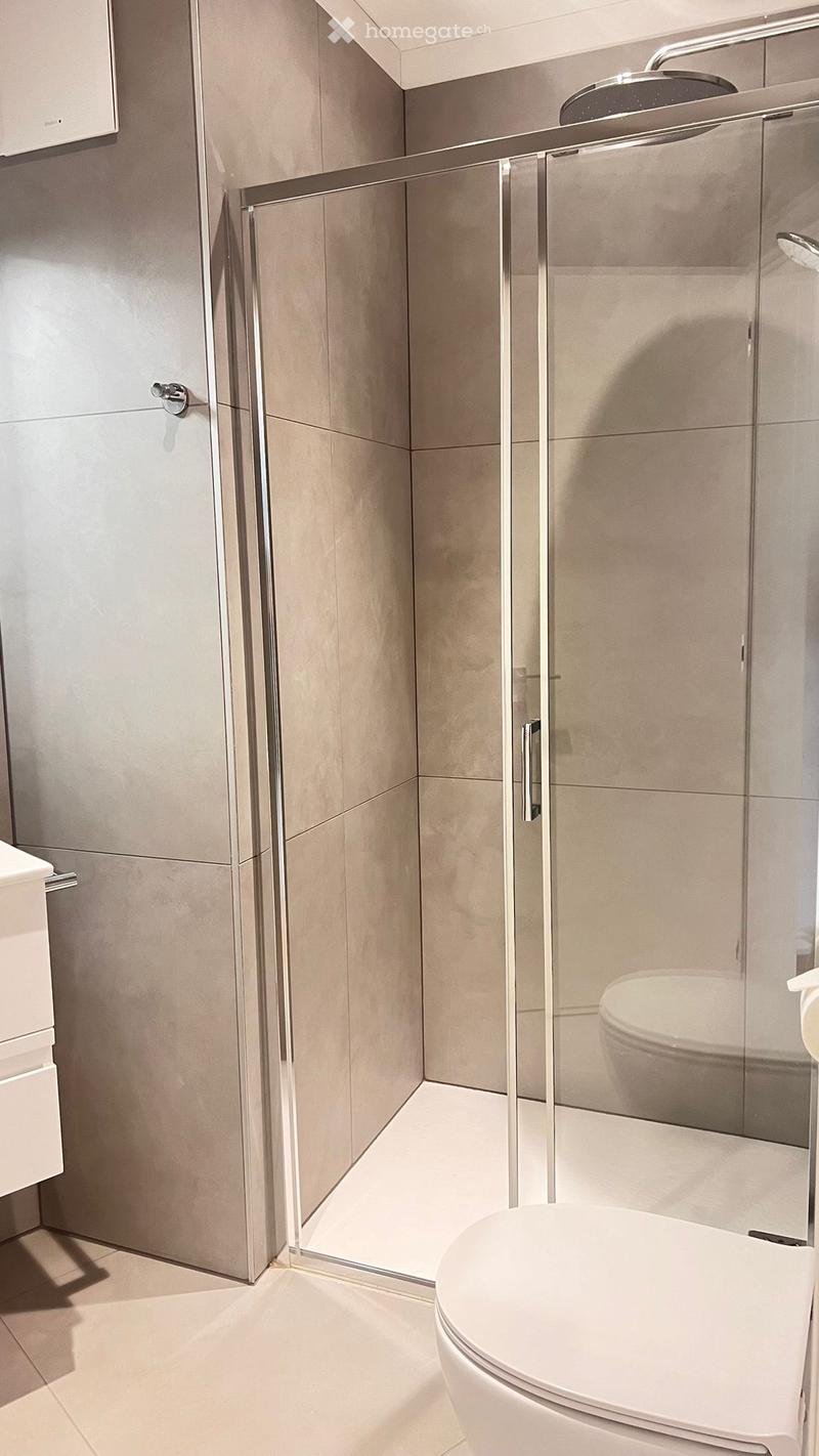 Modern bathroom with a white toilet, glass shower enclosure, and beige tiled walls and floor.