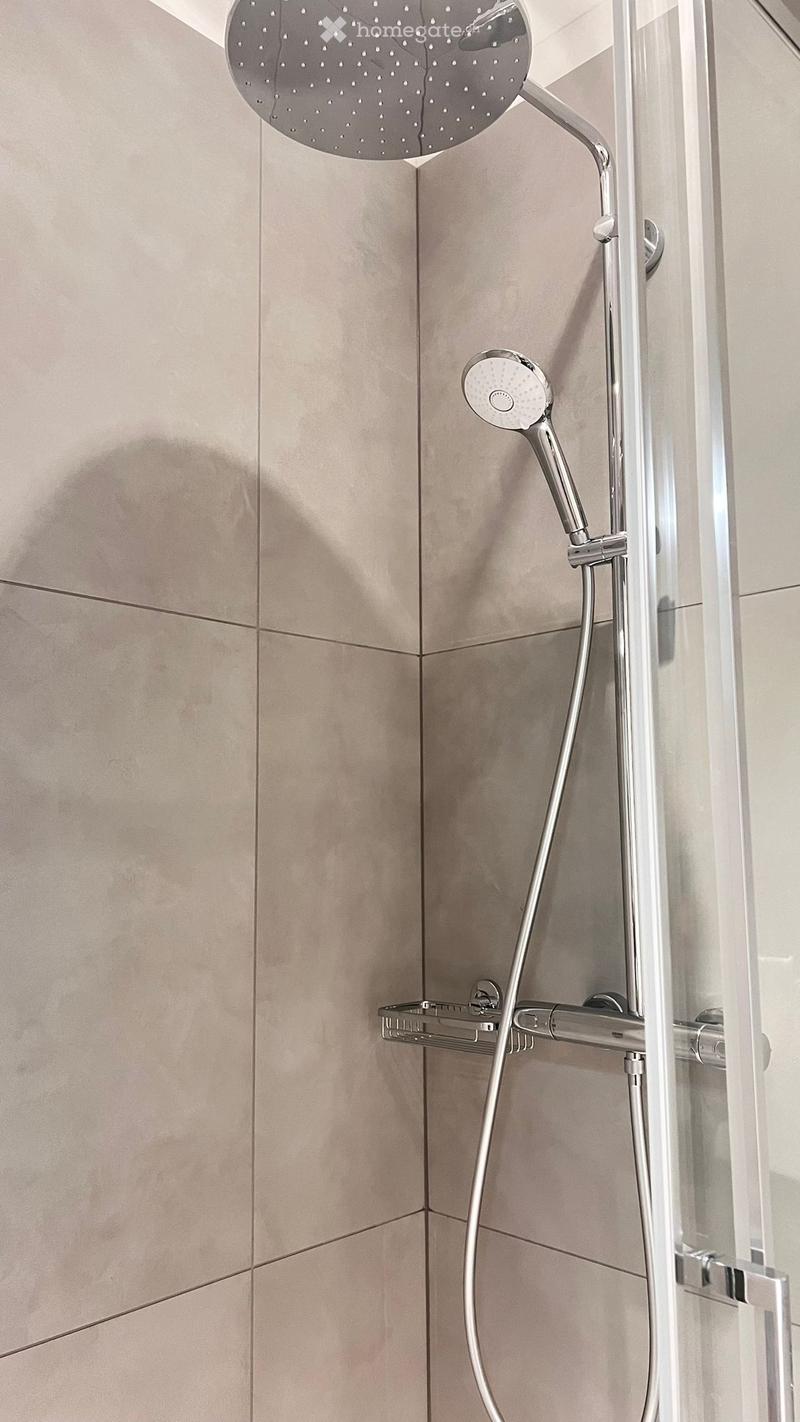 Modern shower area with a large round showerhead, handheld shower attachment, and a built-in shelf for toiletries.