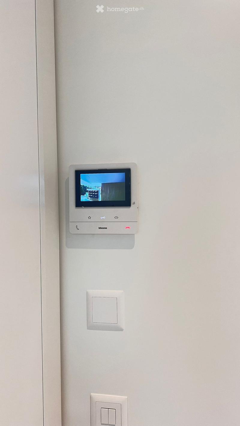 A modern hallway with a sleek intercom system mounted on the wall, featuring a small screen and several buttons.