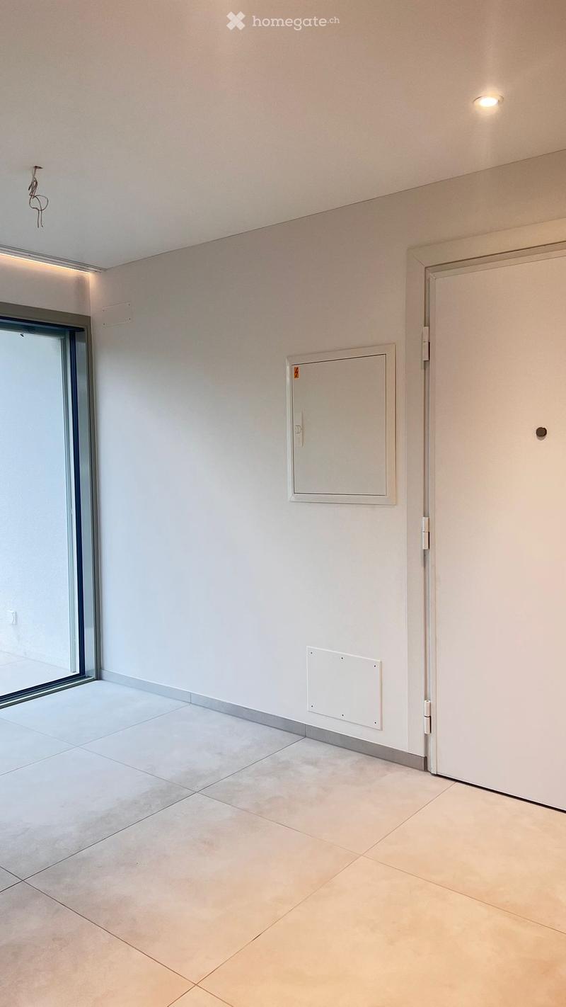 Empty room with white walls, tiled floor, and a large glass door leading outside. No furniture or equipment present.