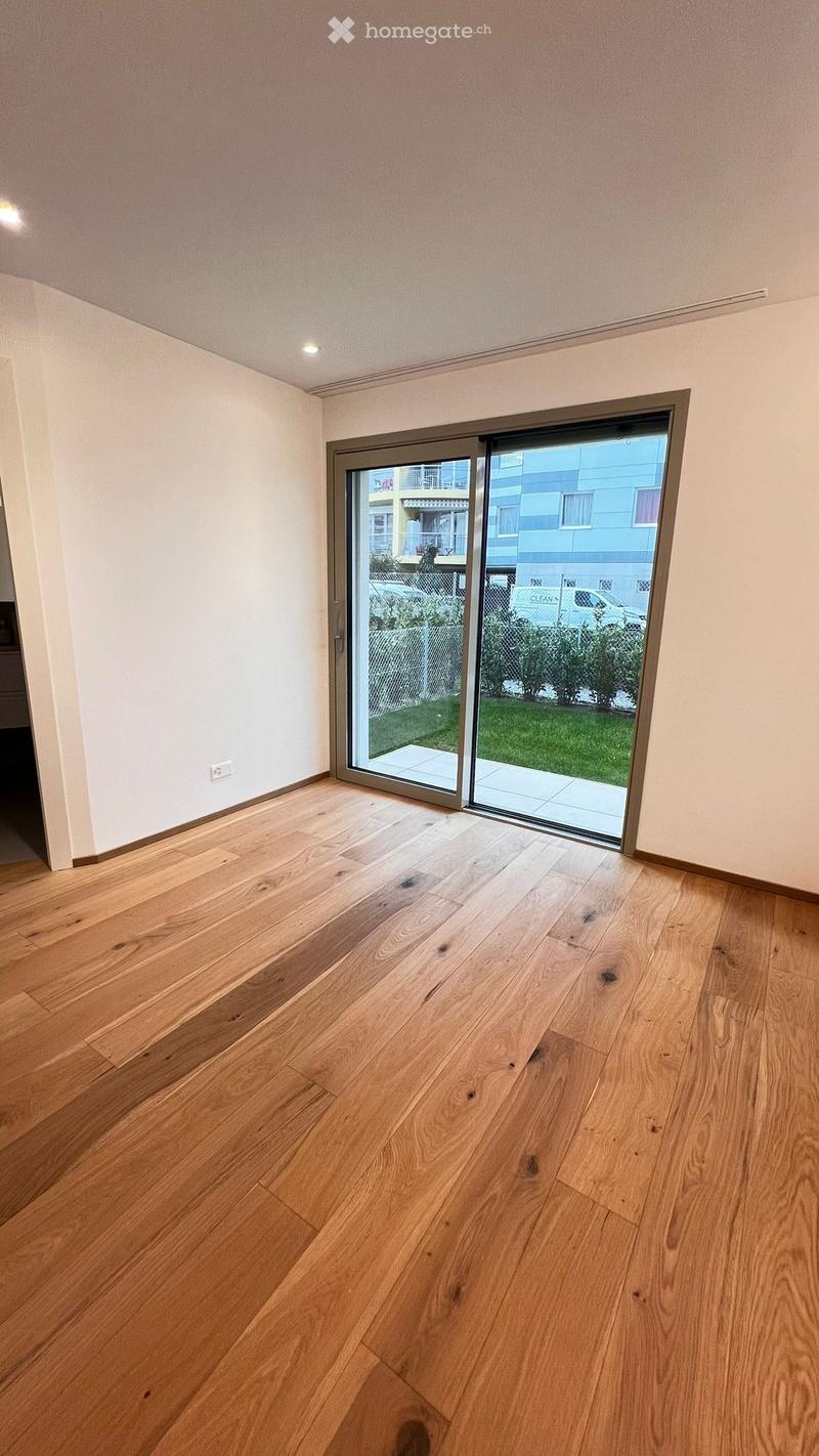 Empty room with wooden flooring and large sliding glass door leading to a balcony or outdoor area. The walls are painted in a light neutral color, and the ceiling has recessed lighting.