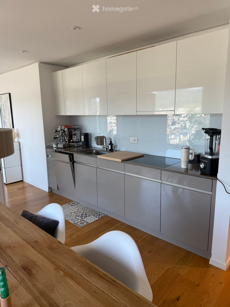 Modern kitchen with white cabinets, stainless steel appliances, wooden floor, and a small dining area with a wooden table and white chairs.