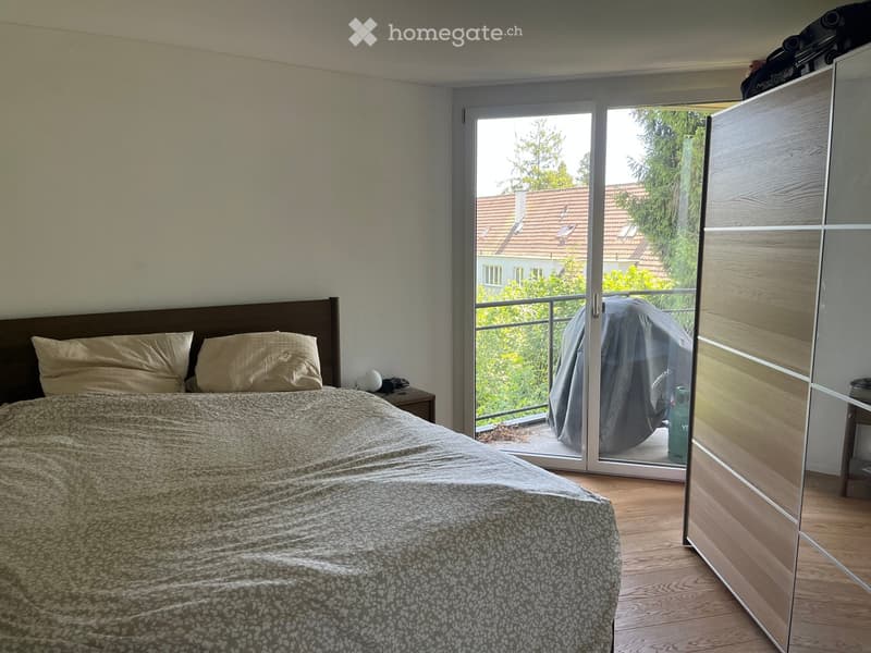Bedroom with a double bed, nightstand, and wardrobe. Large sliding glass door leads to a balcony with outdoor furniture.