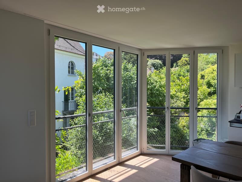 Bright room with large sliding glass doors leading to a balcony, wooden floor, and a small table and chair near the balcony.