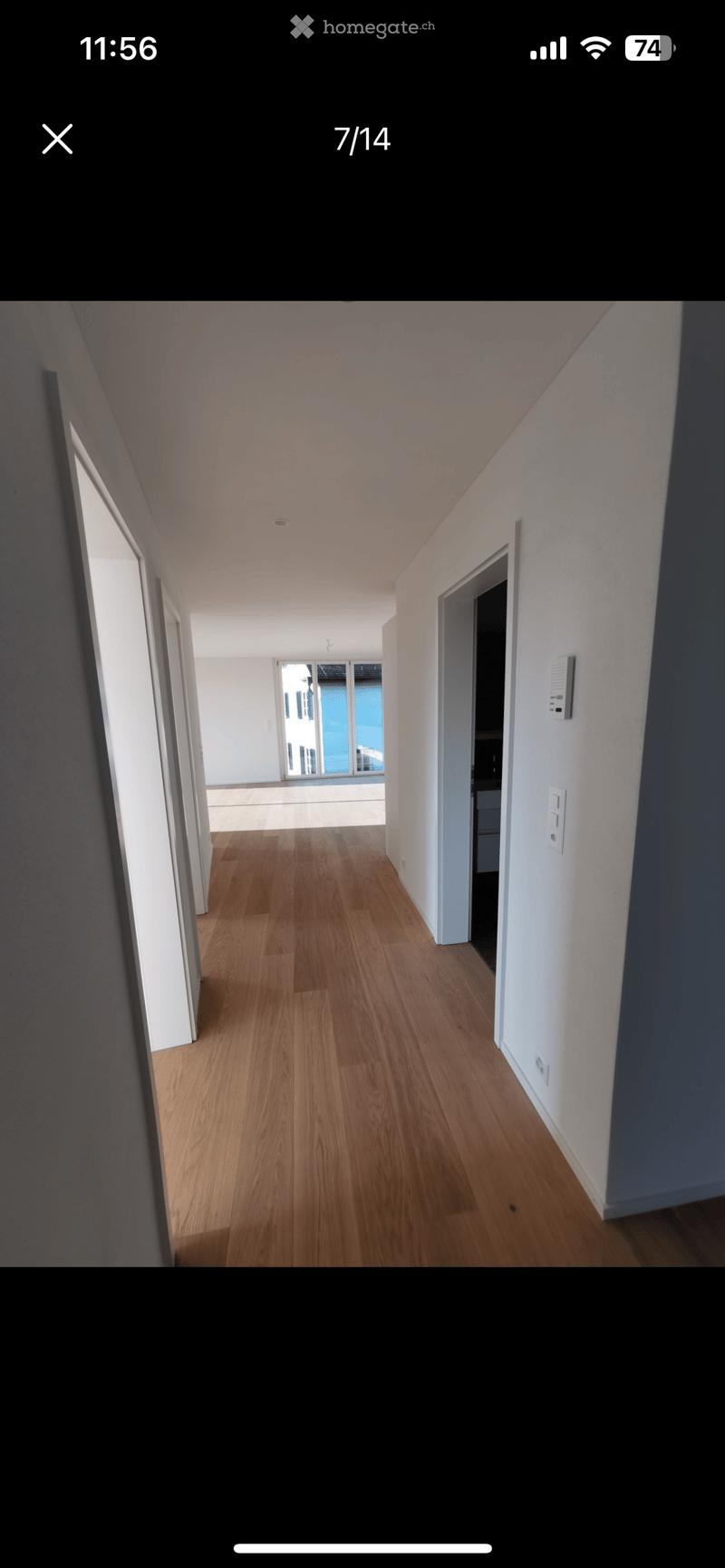 Empty hallway with wooden flooring, white walls, and multiple doors leading to other rooms.