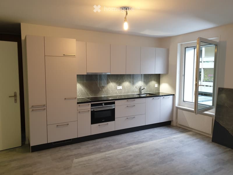Modern kitchen with white cabinets, stainless steel oven, sink, and faucet, featuring a dark backsplash and wooden flooring.