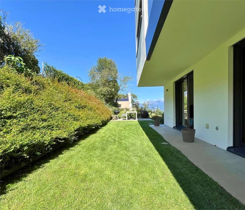 Well-maintained garden with artificial grass, trimmed hedges, and a modern house with large windows and a balcony.