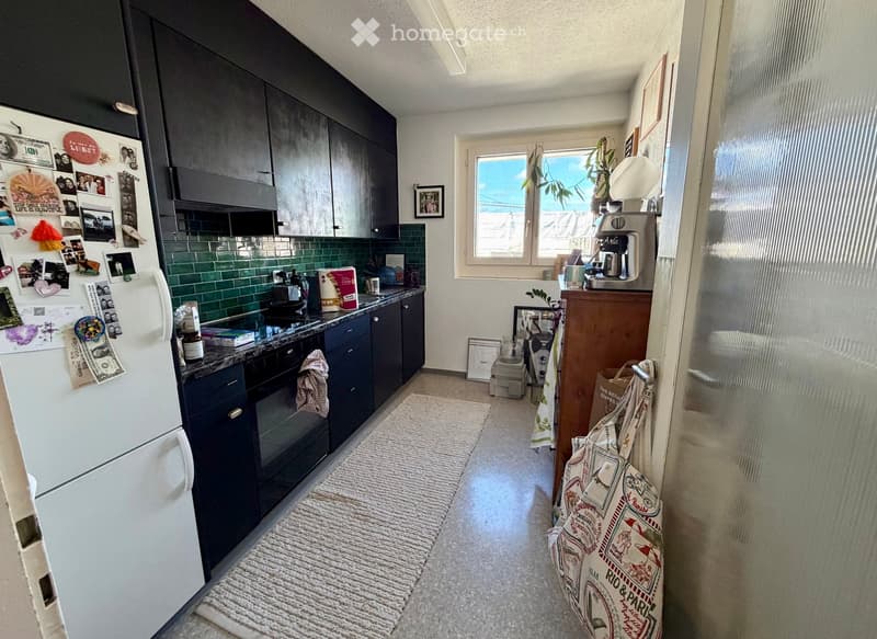 Modern kitchen with dark blue cabinets, white refrigerator, stainless steel appliances, green tiled backsplash, and a coffee maker on a wooden sideboard.