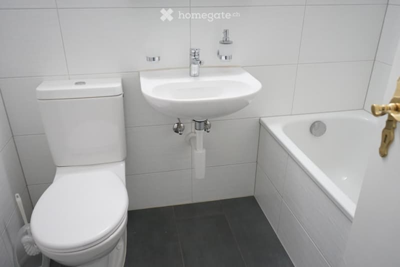 Modern bathroom with white tiles, a toilet, a sink, and a bathtub.