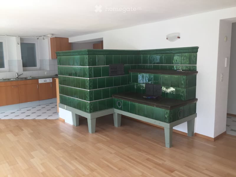 A room with a green tiled bench, wooden flooring, and a kitchen area with cabinets, sink, and dishwasher.