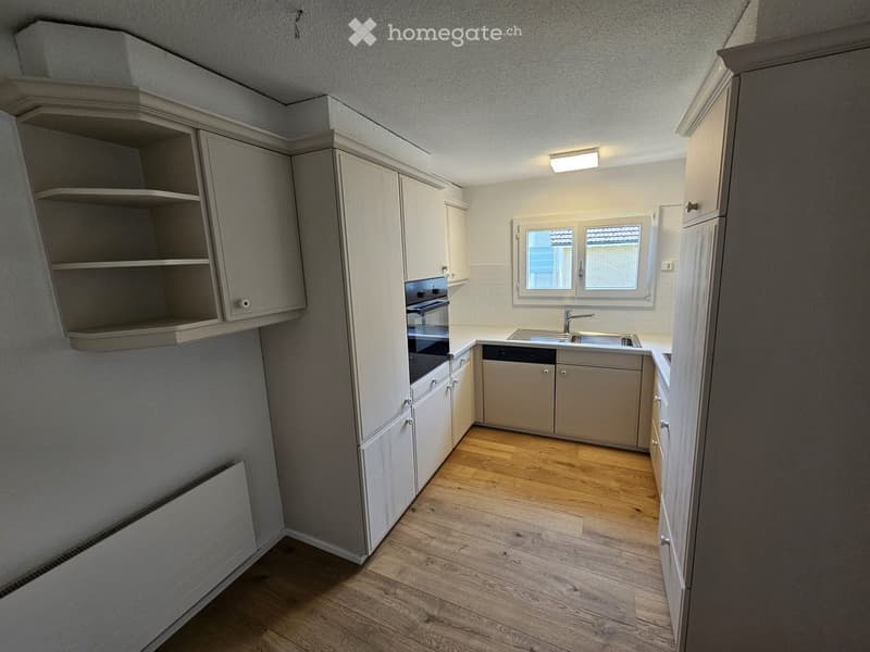 Modern kitchen with light-colored cabinets, wooden flooring, and built-in appliances including an oven and dishwasher.