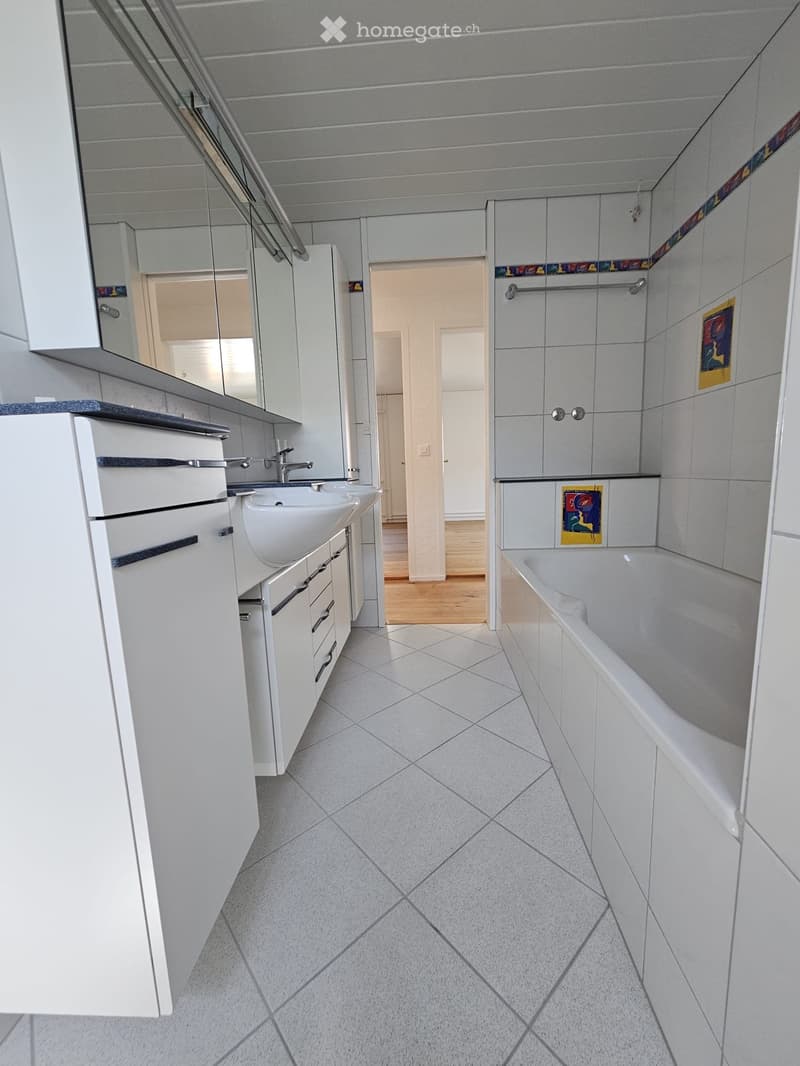 Modern bathroom with white tiles, a double sink, a bathtub, and built-in cabinets.