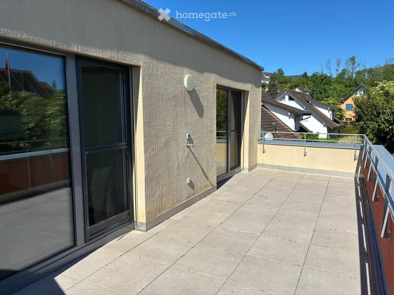 Balcony with tiled floor, glass sliding door, metal railing, and view of surrounding houses and greenery.