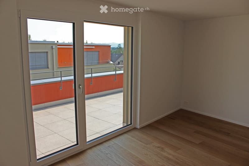 Empty room with wooden flooring and large sliding glass doors leading to a tiled balcony area.