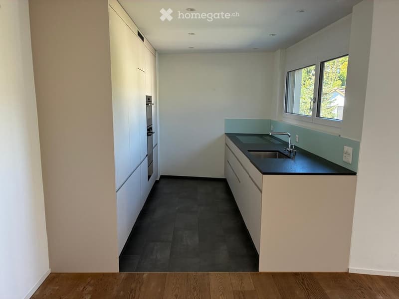 Modern kitchen with white cabinets, black countertops, and a stainless steel sink. The space features a window with a view of greenery outside.