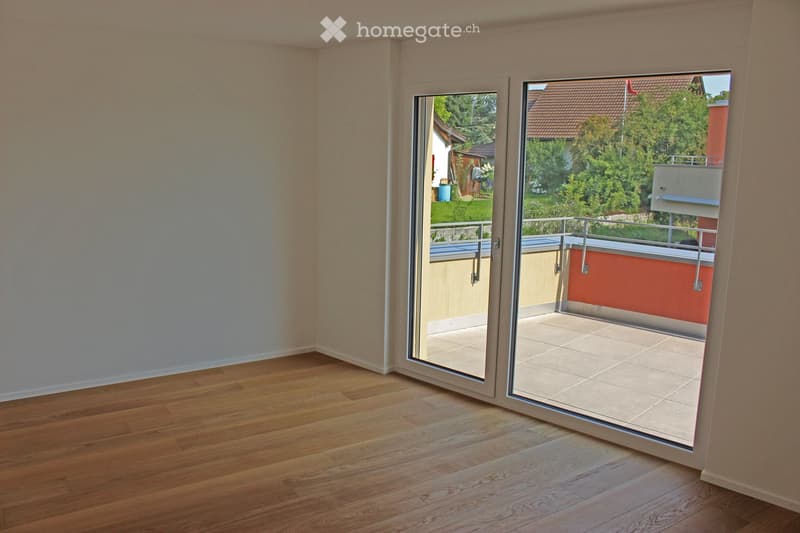 Empty room with wooden flooring and large sliding glass doors leading to a balcony with tiled flooring and a metal railing.