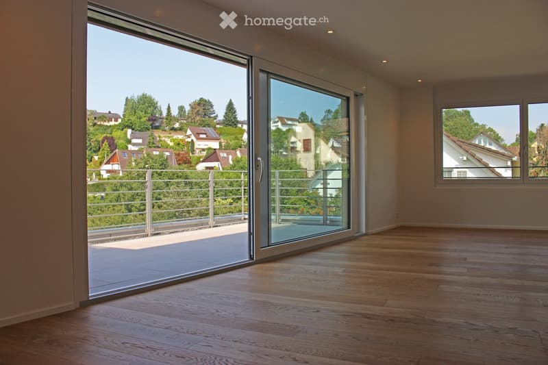 Empty room with wooden flooring, large sliding glass doors leading to a balcony, and a view of a residential area with trees and houses.
