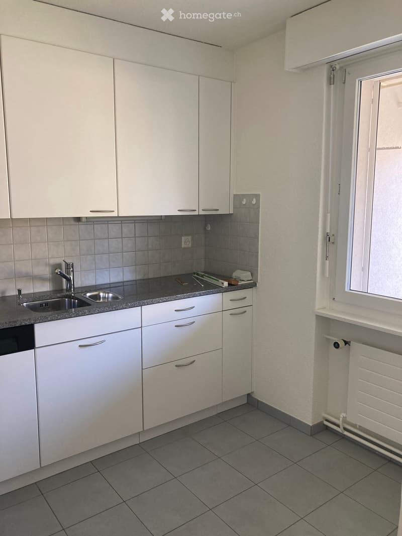 Modern kitchen with white cabinets, grey tiled backsplash, and a stainless steel sink.