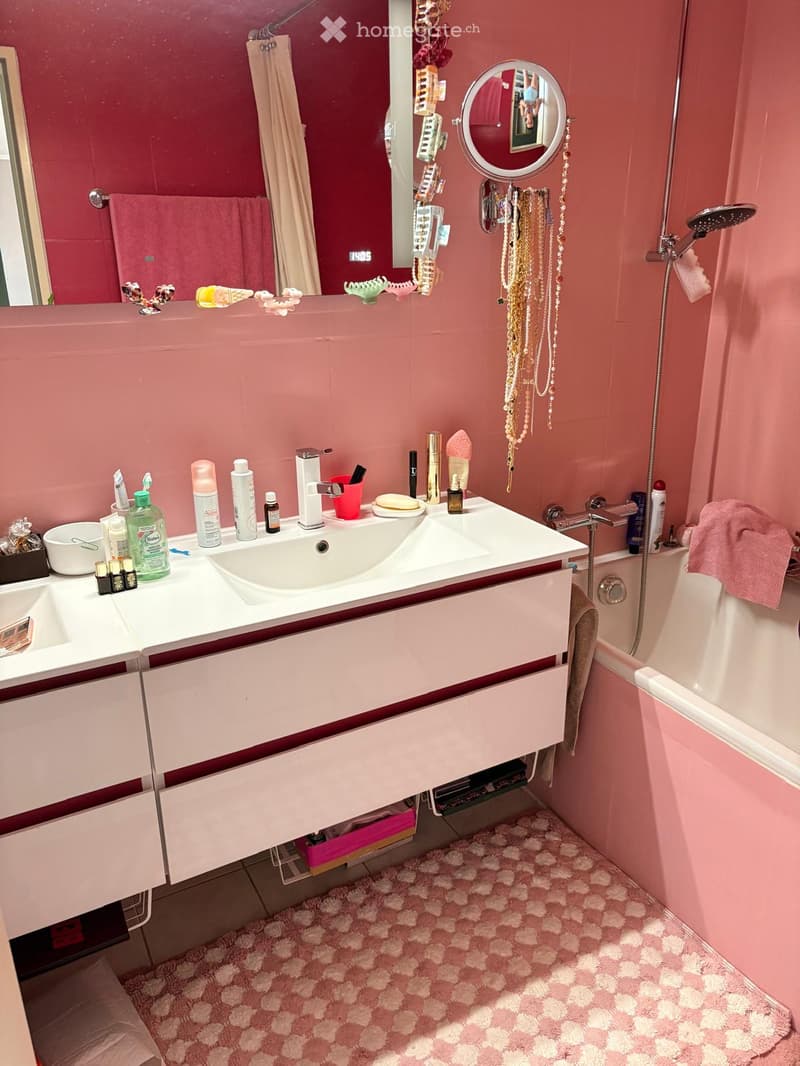 A pink-themed bathroom with a double sink vanity, a bathtub, a large mirror, and various toiletries and decorative items.