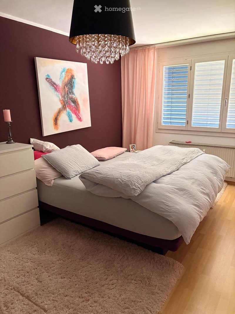 A modern bedroom with a large bed, white bedding, nightstand, chandelier, and artwork on the wall.