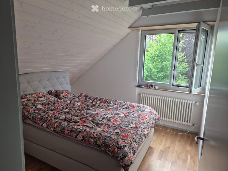 Cozy attic bedroom with wooden slanted ceiling, large windows, and a floral bedspread.