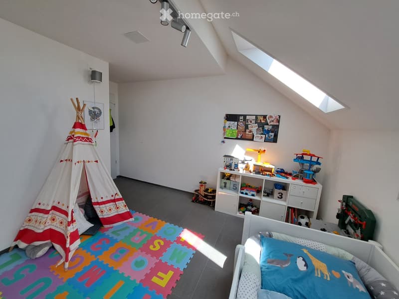 Bright, slanted-ceiling bedroom with a single bed, colorful play mat, toy tent, storage unit, and various toys.