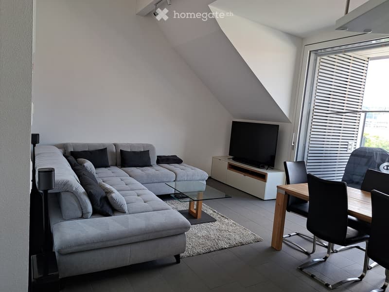 Modern living room with grey sectional sofa, glass coffee table, dining table with chairs, flat-screen TV, and floor lamps.