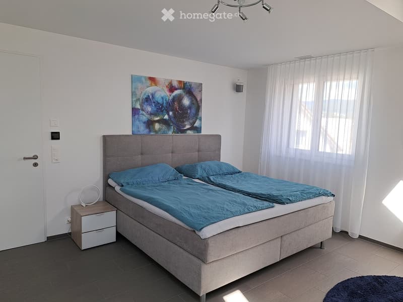 Modern bedroom with a large double bed, nightstand, painting above the bed, and sheer curtains on the window.