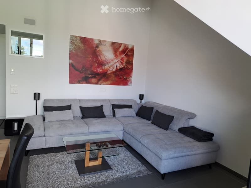 Modern living room with a grey sectional sofa, glass coffee table, black throw, and artwork on the wall.
