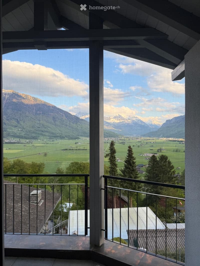 Balcony with metal railing, offering panoramic views of mountains, fields, and a village below.
