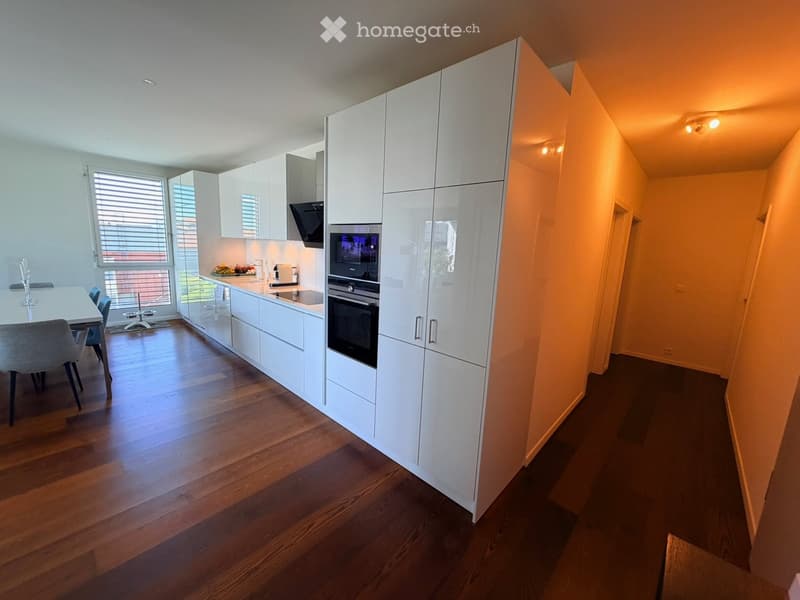 Modern kitchen with white cabinets, stainless steel appliances, wooden flooring, and a dining area with a table and chairs.