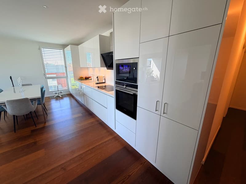 Modern kitchen with white cabinetry, stainless steel appliances, wooden flooring, and a small dining area with a table and chairs.