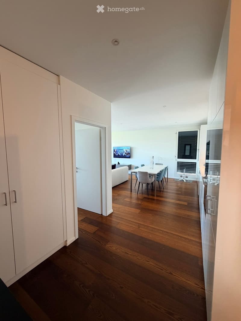 Open-plan living and dining area with wooden flooring, white walls, and modern furniture including a sofa, dining table, and chairs.
